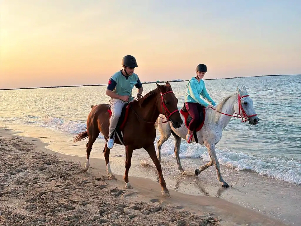 Two riders enjoying a sunset beach horse riding experience along the Ras Al Khaimah coastline, a popular outdoor activity for couples, families, and visitors near Marjan Island.