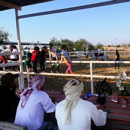 Children participating in a horse riding event at Al Jazeerah Equestrian Club while spectators watch from the sidelines.